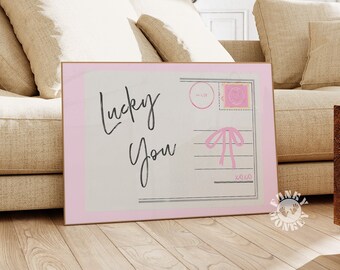 May include: A pink and white postcard with the text "Lucky You" in black script. The postcard has a pink bow and a pink stamp.