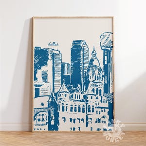 May include: A framed art print featuring a blue ink sketch of the Dallas, Texas skyline. The word "dallas" is written in cursive at the top. The print is in a wooden frame and is displayed against a white wall.