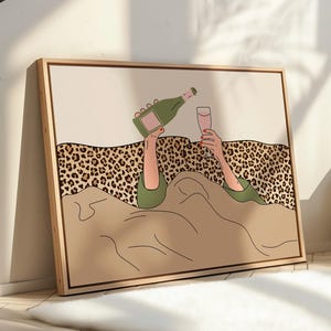 K&ouml;nnte beinhalten: Gerahmter Kunstdruck, der eine Person beim Einschenken von Champagner in ein Glas zeigt. Die Illustration zeigt eine gr&uuml;ne Champagnerflasche, ein rosafarbenes Glas und einen Leopardenmuster-Hintergrund. Das Kunstwerk ist in einem hellen Holzrahmen.