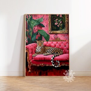May include: A leopard lounges on a pink velvet sofa with gold accents. The sofa is in a room with pink walls and a framed painting of flowers.