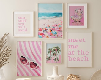 Op de afbeelding: Een witte bank met twee witte rieten manden eronder. Boven de bank hangen zes ingelijste prints aan de wall. De prints tonen strandscenes, schelpen en tekst die zegt "sun surf sea salt sand" en "meet me at the beach".