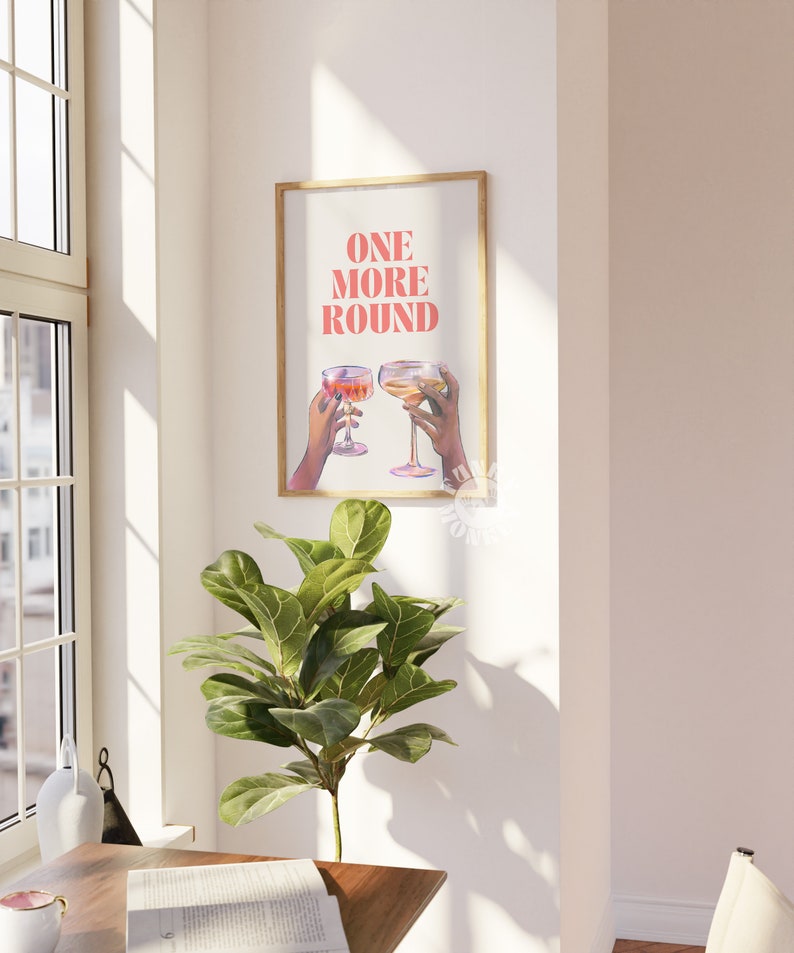 Peut inclure: Une impression encadr&eacute;e avec le texte "ONE MORE ROUND" en lettres roses. Deux mains tiennent des verres de vin, l'un rouge et l'autre blanc, sur un fond blanc.