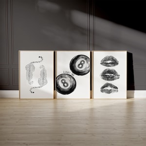 May include: Three black and white framed prints. The left print features a black and white illustration of two leopards. The middle print features two black and white 8-ball illustrations with the text "Lucky Me". The right print features three black and white lips.