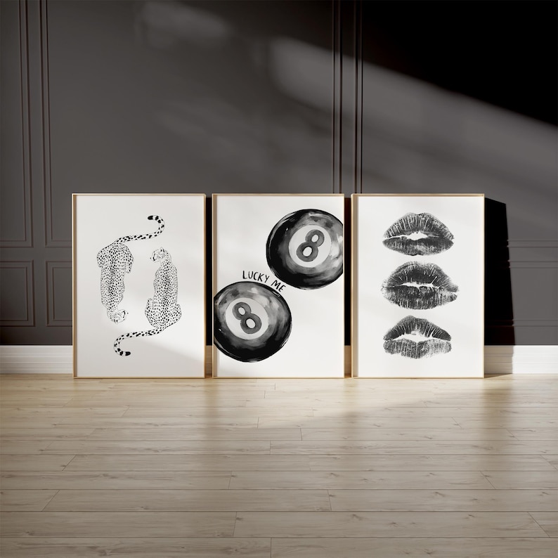 May include: Three black and white framed prints. The left print features a black and white illustration of two leopards. The middle print features two black and white 8-ball illustrations with the text "Lucky Me". The right print features three black and white lips.