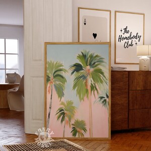 May include: A framed painting of palm trees against a pink and blue sky. The painting is in a wooden frame and is hanging on a wall.
