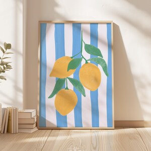 May include: A framed art print featuring a vibrant illustration of lemons on a branch with green leaves. The background has blue and white vertical stripes. The artwork is displayed on a wooden floor.