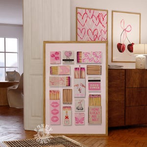 May include: A pink and white framed print with a collage of matchboxes. Each matchbox has a different pink design with text such as "Good Times", "Cheers", and "How Lucky Are We?"