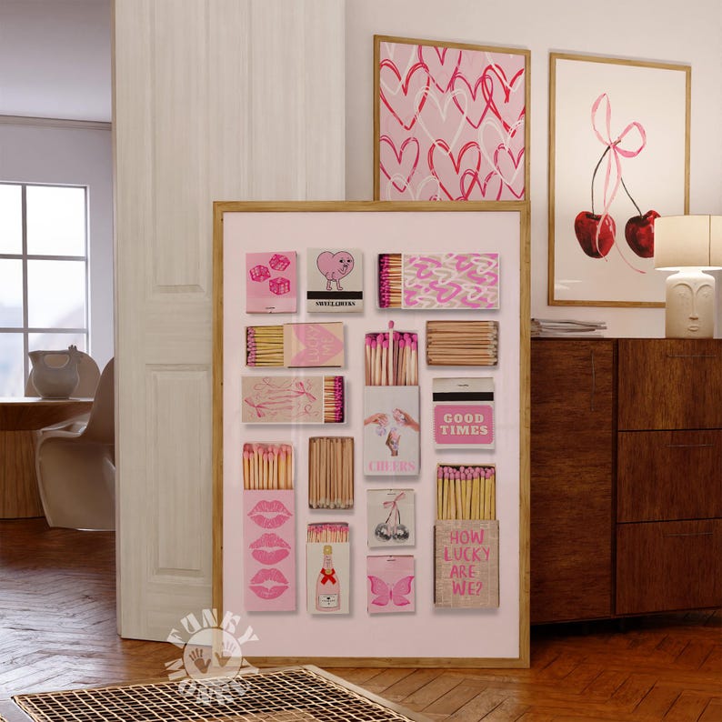 May include: A pink and white framed print with a collage of matchboxes. Each matchbox has a different pink design with text such as "Good Times", "Cheers", and "How Lucky Are We?"