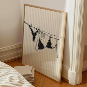 Puede incluir: Una impresi&oacute;n enmarcada con un fondo a rayas que presenta una ilustraci&oacute;n en blanco y negro de dos prendas de ropa interior colgadas de una cuerda para tender la ropa.
