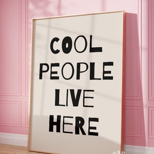 Op de afbeelding: Een ingelijst print met de tekst "COOL PEOPLE LIVE HERE" in zwarte letters op een witte achtergrond.