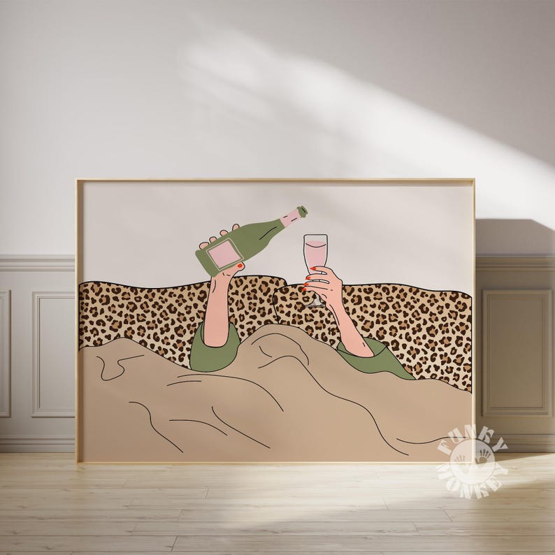 K&ouml;nnte beinhalten: Ein gerahmter Kunstdruck zeigt eine Person, die Champagner in ein Glas gie&szlig;t. Die Illustration zeigt eine gr&uuml;ne Champagnerflasche, ein Glas rosa Fl&uuml;ssigkeit und H&auml;nde mit rotem Nagellack. Der Hintergrund umfasst einen Leopardenmuster und eine beige Decke.