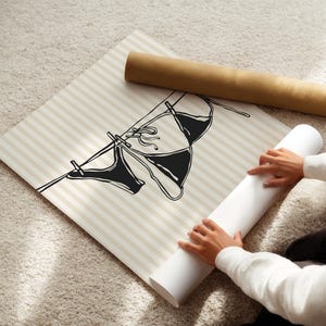 Puede incluir: Una ilustraci&oacute;n en blanco y negro de dos trajes de ba&ntilde;o colgados de una cuerda para tender la ropa. La ilustraci&oacute;n est&aacute; impresa sobre un fondo a rayas beige y blanco.