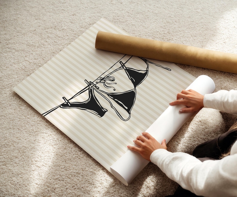 Puede incluir: Una ilustraci&oacute;n en blanco y negro de dos trajes de ba&ntilde;o colgados de una cuerda para tender la ropa. La ilustraci&oacute;n est&aacute; impresa sobre un fondo a rayas beige y blanco.
