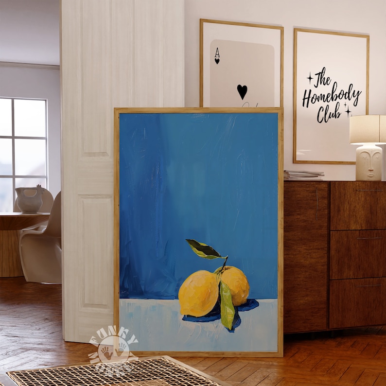 May include: A painting of two lemons with green leaves on a blue background. The lemons are yellow and the leaves are green. The painting is framed in a wooden frame.