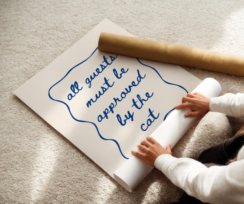 May include: A white poster with blue text that reads "all guests must be approved by the cat". A person is rolling up the poster.