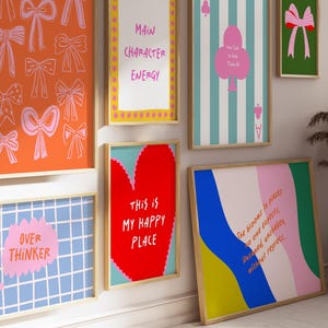Puede incluir: Una colecci&oacute;n de impresiones art&iacute;sticas enmarcadas con varios dise&ntilde;os y texto. Una impresi&oacute;n presenta lazos naranjas, otra dice "Main Character Energy", y una tercera dice "This is My Happy Place". Otras impresiones incluyen una cuadr&iacute;cula azul con "Over Thinker" y un dise&ntilde;o abstracto colorido.