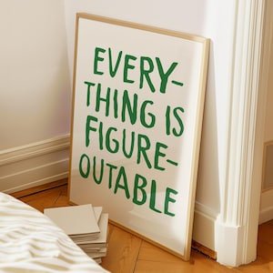 Op de afbeelding: Een ingelijste kunstprint met de tekst "EVERYTHING IS FIGURE-OUTABLE" in groen, leunend tegen een muur. De lijst is goudkleurig en de achtergrond is gebroken wit. De print staat op een houten vloer.