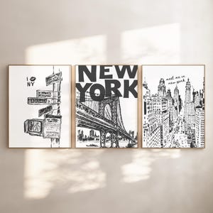 May include: Set of three framed black and white art prints. The prints depict New York City scenes, including street signs, the Brooklyn Bridge, and a cityscape. The prints are in gold frames.