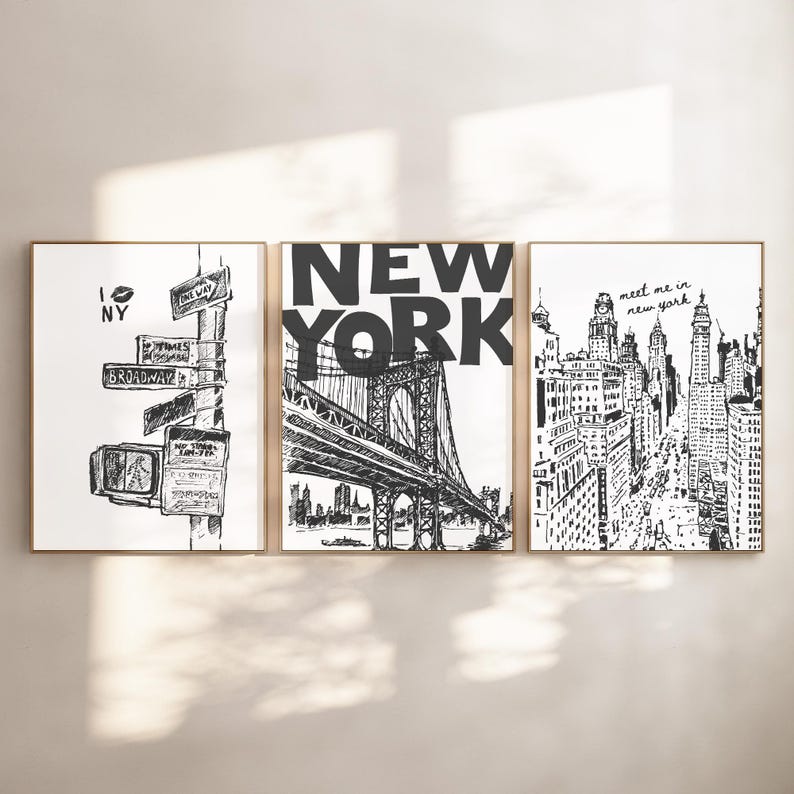 May include: Set of three framed black and white art prints. The prints depict New York City scenes, including street signs, the Brooklyn Bridge, and a cityscape. The prints are in gold frames.