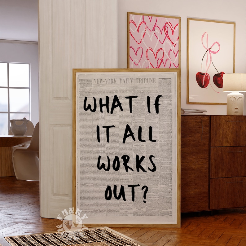 Op de afbeelding: Een ingelijst drukwerk met een krantenachtergrond en de tekst "WHAT IF IT ALL WORKS OUT?" in zwarte letters. De print hangt aan een muur in een kamer met een houten vloer en een witte deur.