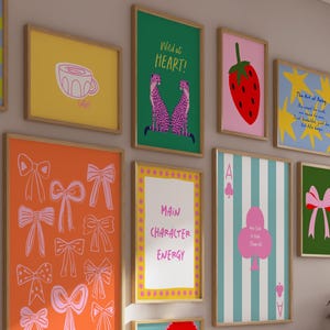 Puede incluir: Una colecci&oacute;n de impresiones art&iacute;sticas enmarcadas con varios dise&ntilde;os. Las impresiones presentan una taza amarilla, una fresa roja, lazos rosas y un fondo verde con un lazo rosa. Otras impresiones incluyen el texto "Wild at Heart!" y "Main Character Energy."