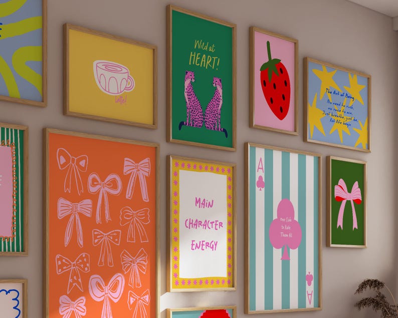 Puede incluir: Una colecci&oacute;n de impresiones art&iacute;sticas enmarcadas con varios dise&ntilde;os. Las impresiones presentan una taza amarilla, una fresa roja, lazos rosas y un fondo verde con un lazo rosa. Otras impresiones incluyen el texto "Wild at Heart!" y "Main Character Energy."