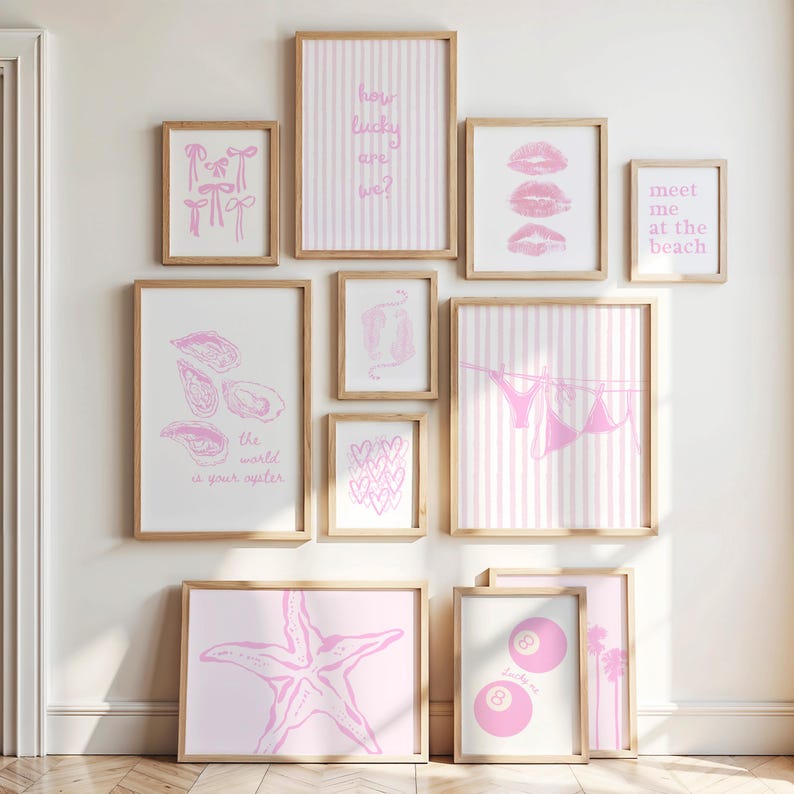 May include: A collection of framed art prints in various sizes, featuring pink designs on white backgrounds. The prints include text, bows, hearts, lips, a starfish, and an 8-ball. The frames are made of light-colored wood.
