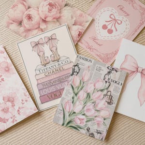 May include: A collection of five rectangular art prints featuring pink and white themes. Designs include a stack of designer books with high heels, a bouquet of pink tulips over newspaper text, a large pink bow, a heart with cherries, and pink peonies.