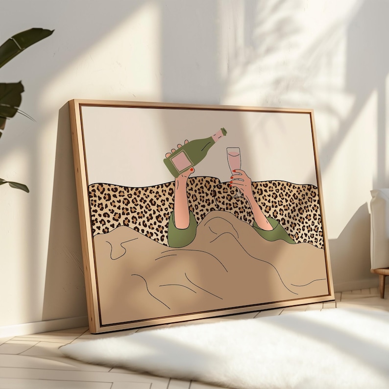 K&ouml;nnte beinhalten: Gerahmter Kunstdruck, der eine Person beim Einschenken von Champagner in ein Glas zeigt. Die Illustration zeigt eine gr&uuml;ne Champagnerflasche, ein rosafarbenes Glas und einen Leopardenmuster-Hintergrund. Das Kunstwerk ist in einem hellen Holzrahmen.