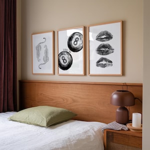 May include: Three framed black and white prints on a light beige wall above a wooden headboard. The prints feature a stylized image of a leopard, a black and white 8-ball with the text "Lucky Me", and three black and white lips.