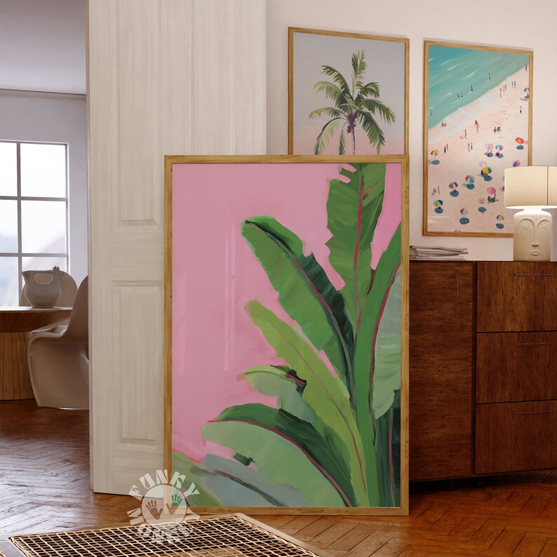 May include: A framed print of a pink background with green banana leaves. The leaves are painted in a stylized, abstract style.