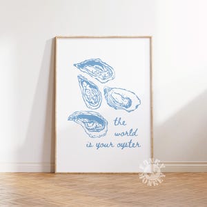 May include: A framed print featuring four blue oyster illustrations on a white background. The phrase "the world is your oyster" is written in blue script below the oysters. The artwork is displayed on a wooden floor.