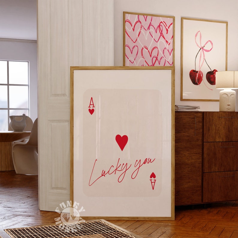Op de afbeelding: Een witte ingelijste print met een rood aas harten speelkaartontwerp. De kaart heeft een rood hart in het midden en de tekst "lucky you" in cursief.
