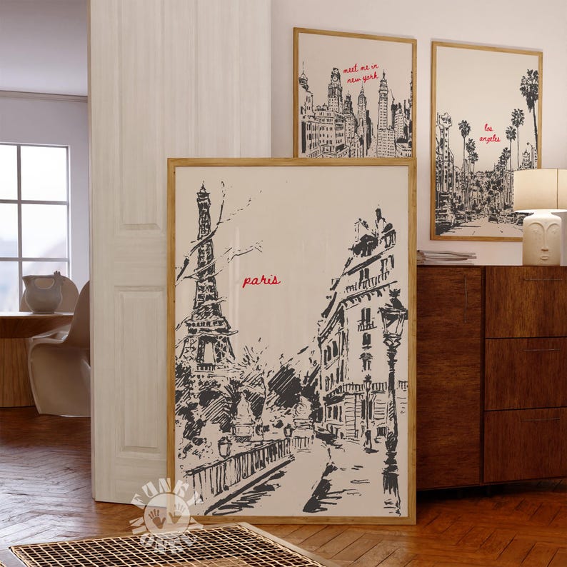 May include: A black and white sketch of the Eiffel Tower and a Parisian street scene. The image is framed in a light wood frame and the word "paris" is written in red lettering.
