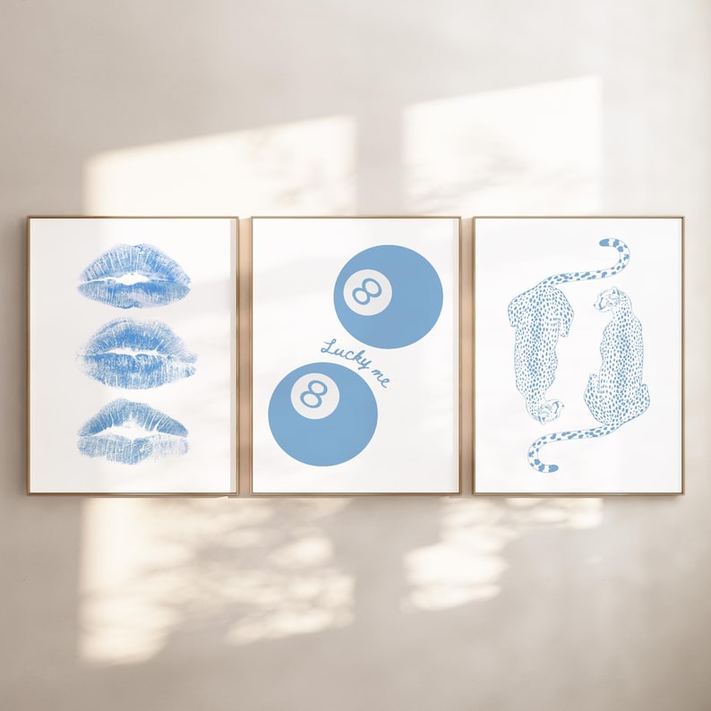 May include: Three framed art prints with gold frames. The prints feature blue designs on a white background. One print shows three blue lip imprints. Another has two blue 8-ball designs with the text "Lucky me". The third print depicts two blue cheetahs.