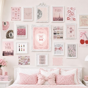May include: A gallery wall arrangement featuring various pink-themed art prints in white frames, including images of cherries, Paris, lip prints, and fashion items, displayed above a bed with pink leopard print pillows and a central bow-shaped pillow.