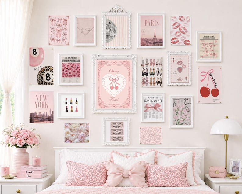 May include: A gallery wall arrangement featuring various pink-themed art prints in white frames, including images of cherries, Paris, lip prints, and fashion items, displayed above a bed with pink leopard print pillows and a central bow-shaped pillow.