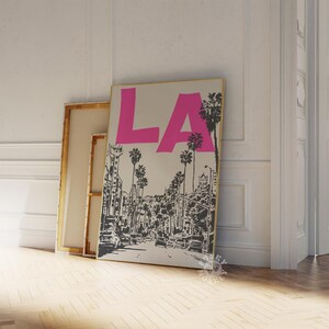 May include: A black and white illustration of a city street with palm trees and the word 'LA' in pink letters on a beige background.