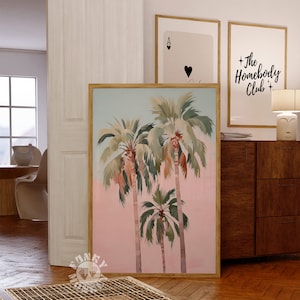 May include: A framed print of three palm trees against a pink and blue sky. The print is in a wooden frame and is hanging on a wall.