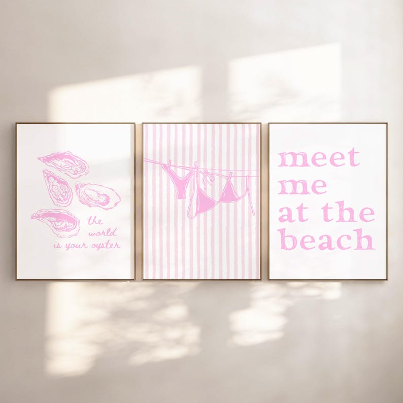 May include: Three framed prints with pink designs. One print features oyster illustrations and the text "the world is your oyster." Another shows a pink bikini hanging on a clothesline against pink stripes. The third print says "meet me at the beach."