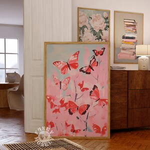 Op de afbeelding: Een ingelijst schilderij van roze vlinders op een roze en blauwe achtergrond. De vlinders bevinden zich in verschillende posities en maten. Het schilderij is in een houten lijst.