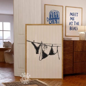 Puede incluir: Una ilustraci&oacute;n en blanco y negro de un bikini colgado de una cuerda para tender la ropa. La ilustraci&oacute;n est&aacute; sobre un fondo beige con rayas verticales. El texto "Meet me at the beach" es visible en el fondo.