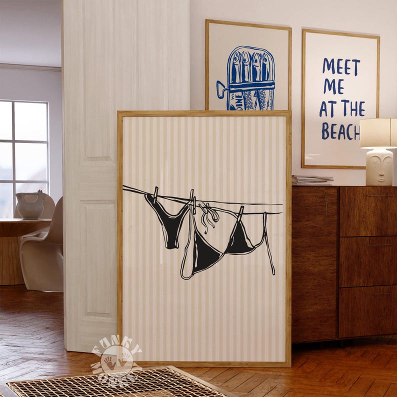 Puede incluir: Una ilustraci&oacute;n en blanco y negro de un bikini colgado de una cuerda para tender la ropa. La ilustraci&oacute;n est&aacute; sobre un fondo beige con rayas verticales. El texto "Meet me at the beach" es visible en el fondo.