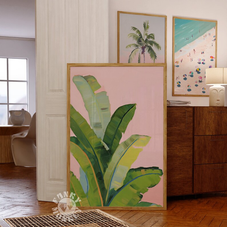 May include: A pink and green tropical leaf painting with a wooden frame. The painting is hanging on a wall in a room with a wooden floor and a white door.