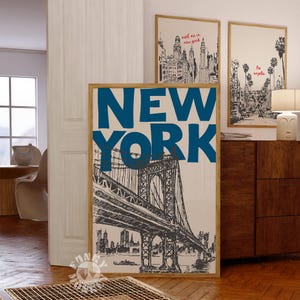 May include: A framed print with a beige background and a blue and white illustration of the Brooklyn Bridge in New York City. The text "NEW YORK" is in large blue letters above the bridge.
