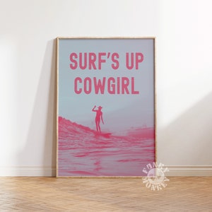 May include: A pink and white poster with the text "SURF'S UP COWGIRL" in pink letters. The poster features a silhouette of a woman in a cowboy hat surfing on a wave.