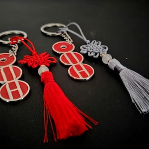 May include: Keychains with silver rings and red and white circular pendants. One keychain has a red tassel, another has a red knot, and the third has a gray tassel. The pendants have the letter "H" on them.