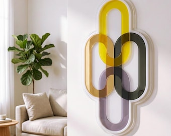 May include: Abstract wall art with overlapping oval shapes in yellow, gold, brown, dark green, and purple. The artwork is framed in white and mounted on a white wall. A living room setting with a plant and sofa is visible.