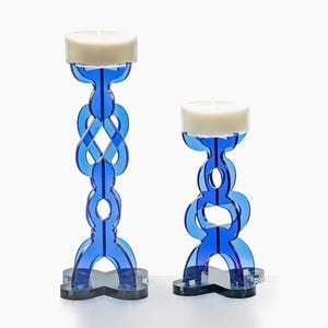 Peut inclure: Deux bougeoirs bleus en acrylique avec un design entrelacé. Chaque support a une bougie blanche sur le dessus. Les bases sont noires. Le plus grand mesure environ 30 cm de haut, et le plus petit environ 20 cm.