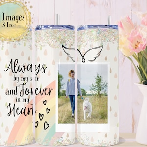 May include: A white tumbler with a lid and straw, featuring a photo of a person walking a dog. The tumbler has a design with the text "Always by my side and Forever in my Heart" and a rainbow. The top is decorated with glitter.